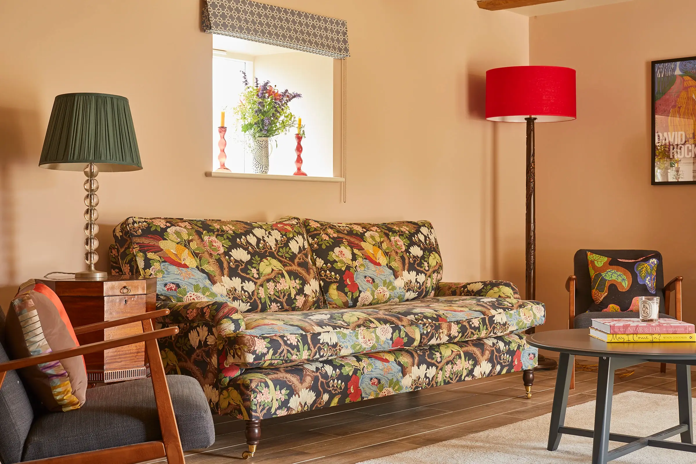 Living room with a floral sofa, red lampshade, grey chair, coffee table, and wall art.