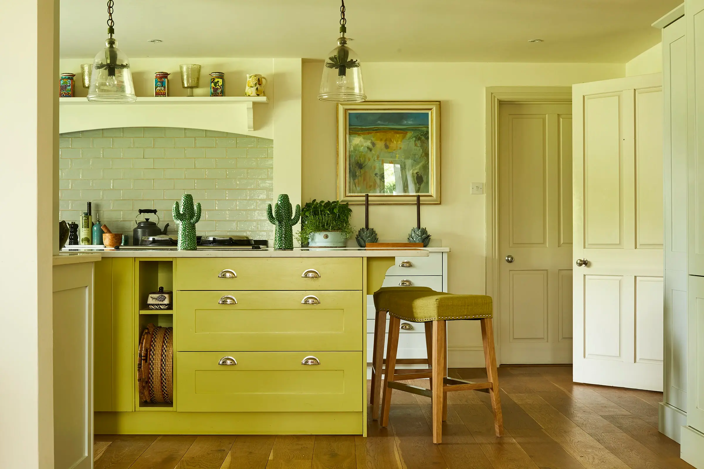 Kitchen with lime cabinets, barstool, wooden floor, and hanging lights; art and cactus decor visible.