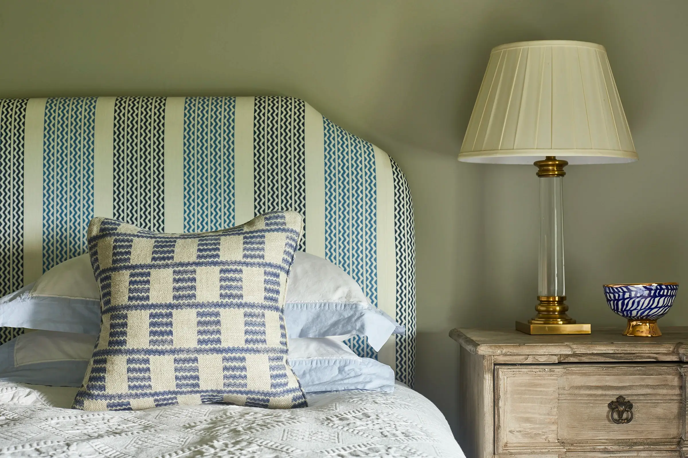 Bedroom with striped headboard, patterned pillow, wooden nightstand, and table lamp.