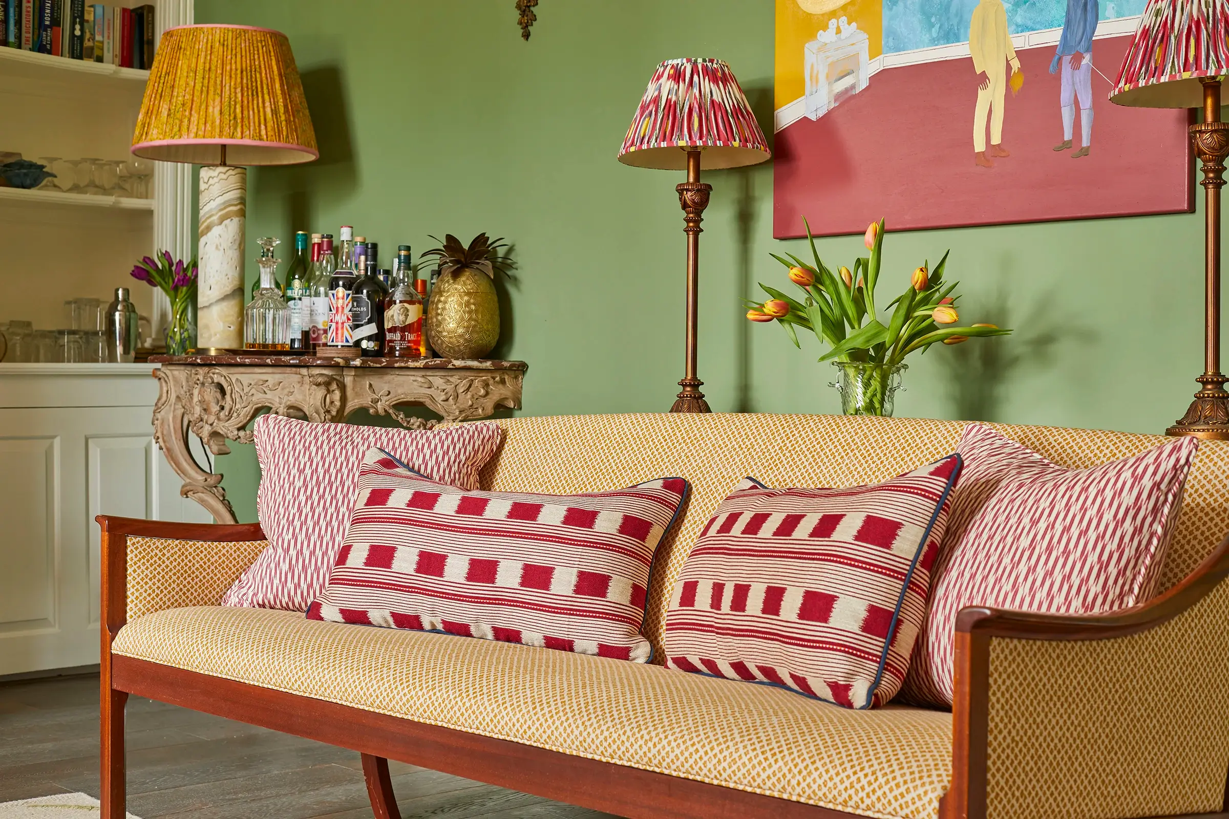 Living room with patterned sofa, decorative pillows and colorful artwork on a green wall.