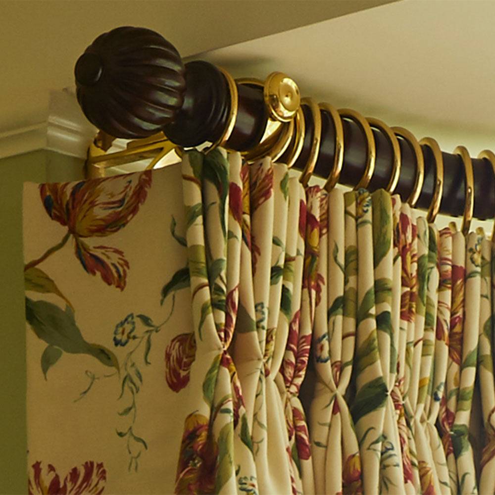 Floral curtains hanging on a dark wooden rod with gold rings and decorative end cap.