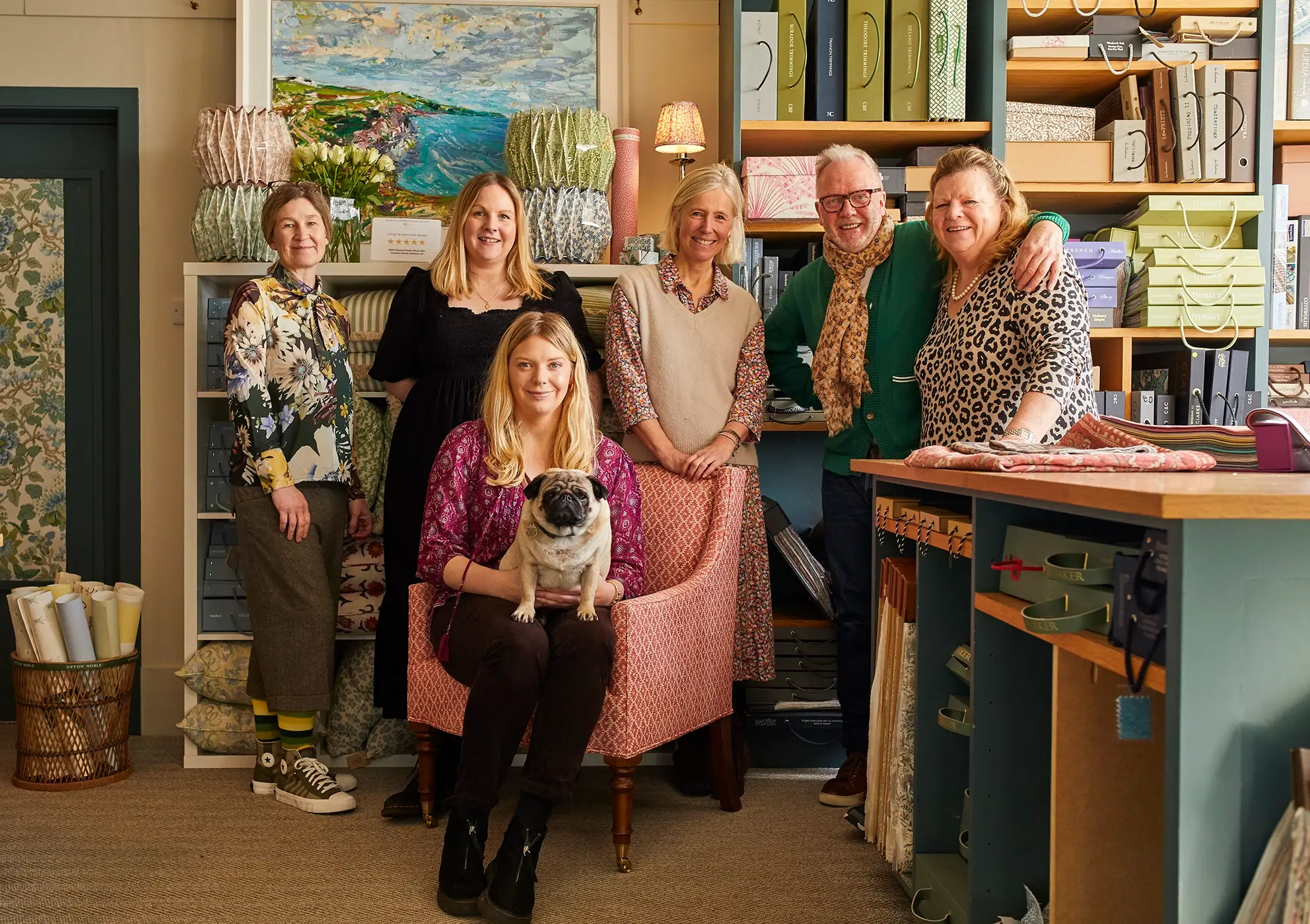 Six people and a dog in a fabric store with shelves and rolls of fabric in the background.