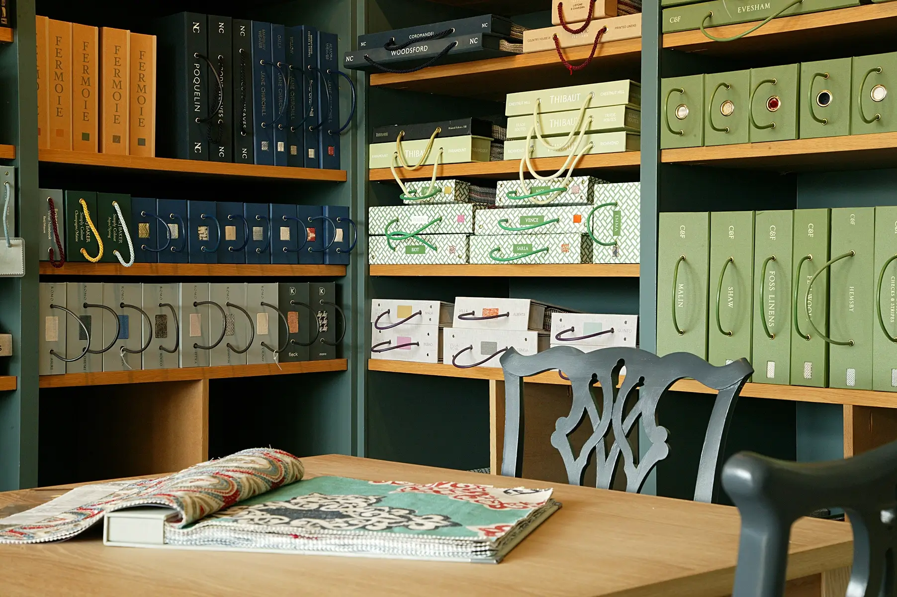 A room with shelves of colorful fabric sample books and a wooden table with an open book.