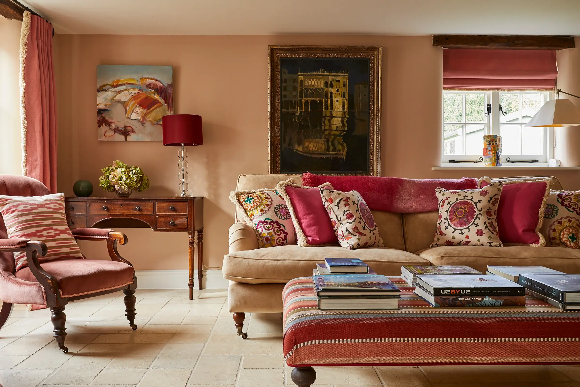 Cozy living room with a beige sofa, colorful cushions, matching armchair, and a wooden coffee table with books.